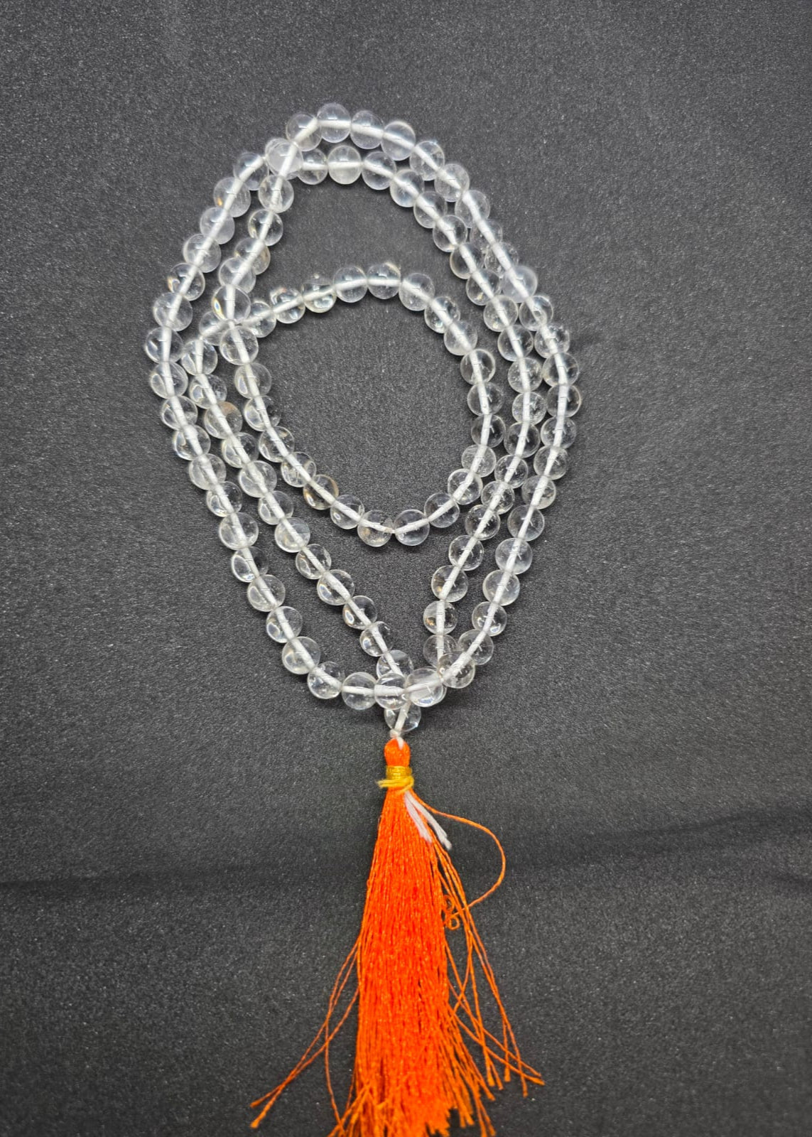 Clear Quartz Crystal Mala for Jaap- 108 beads on a dark background with an orange tassel.